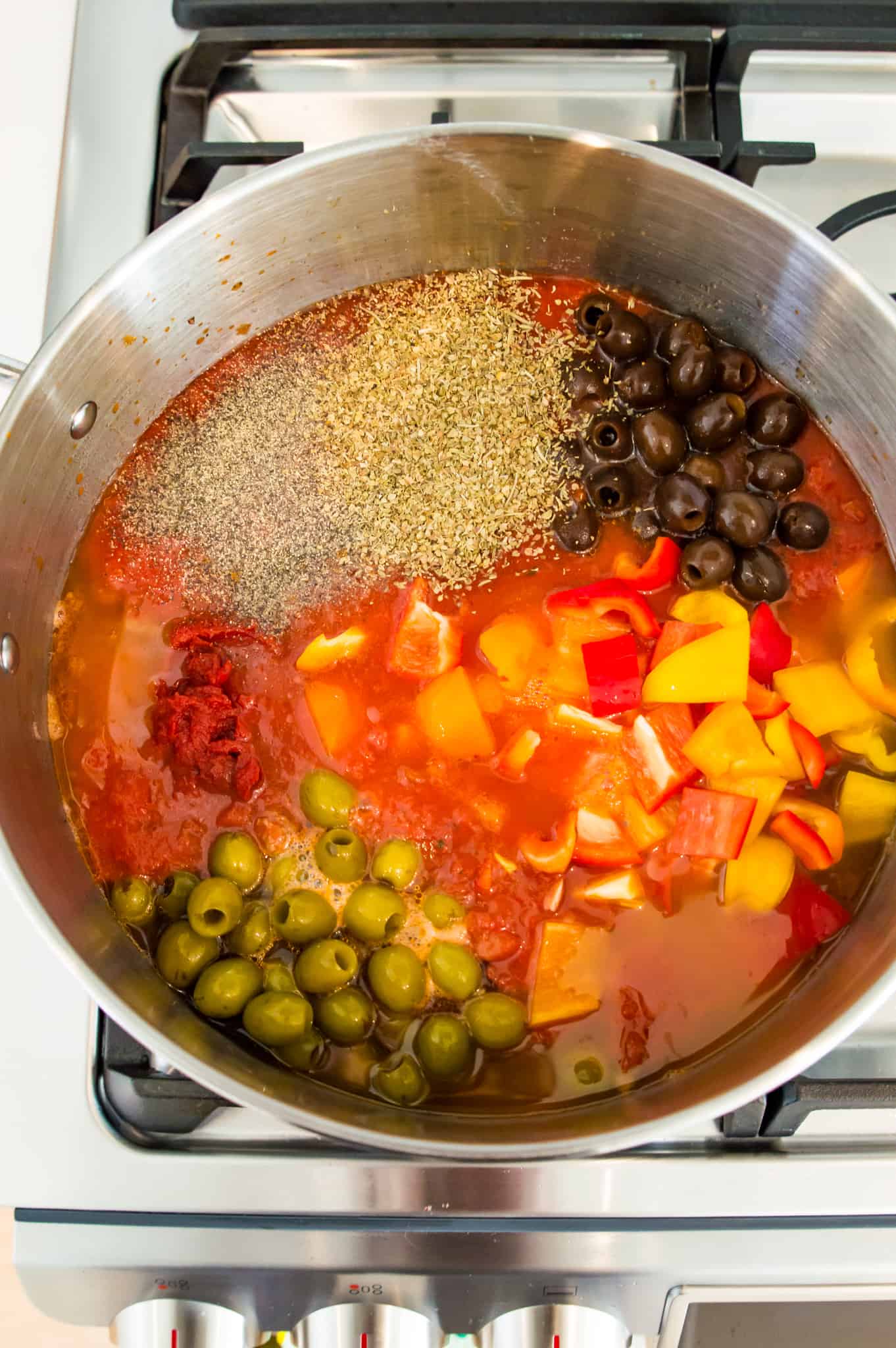 A pot with tomato sauce, olives, spices and ground beef in it.