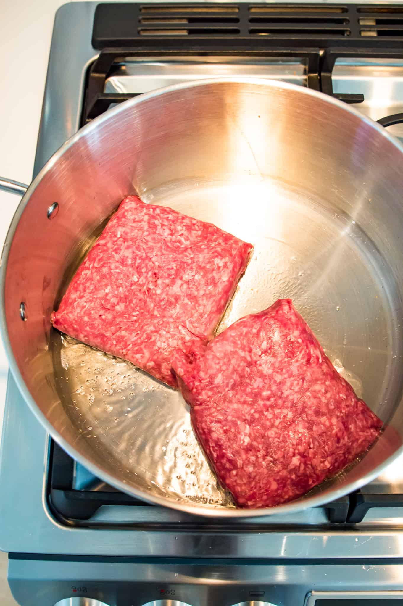 A pot with uncooked ground beef in it.