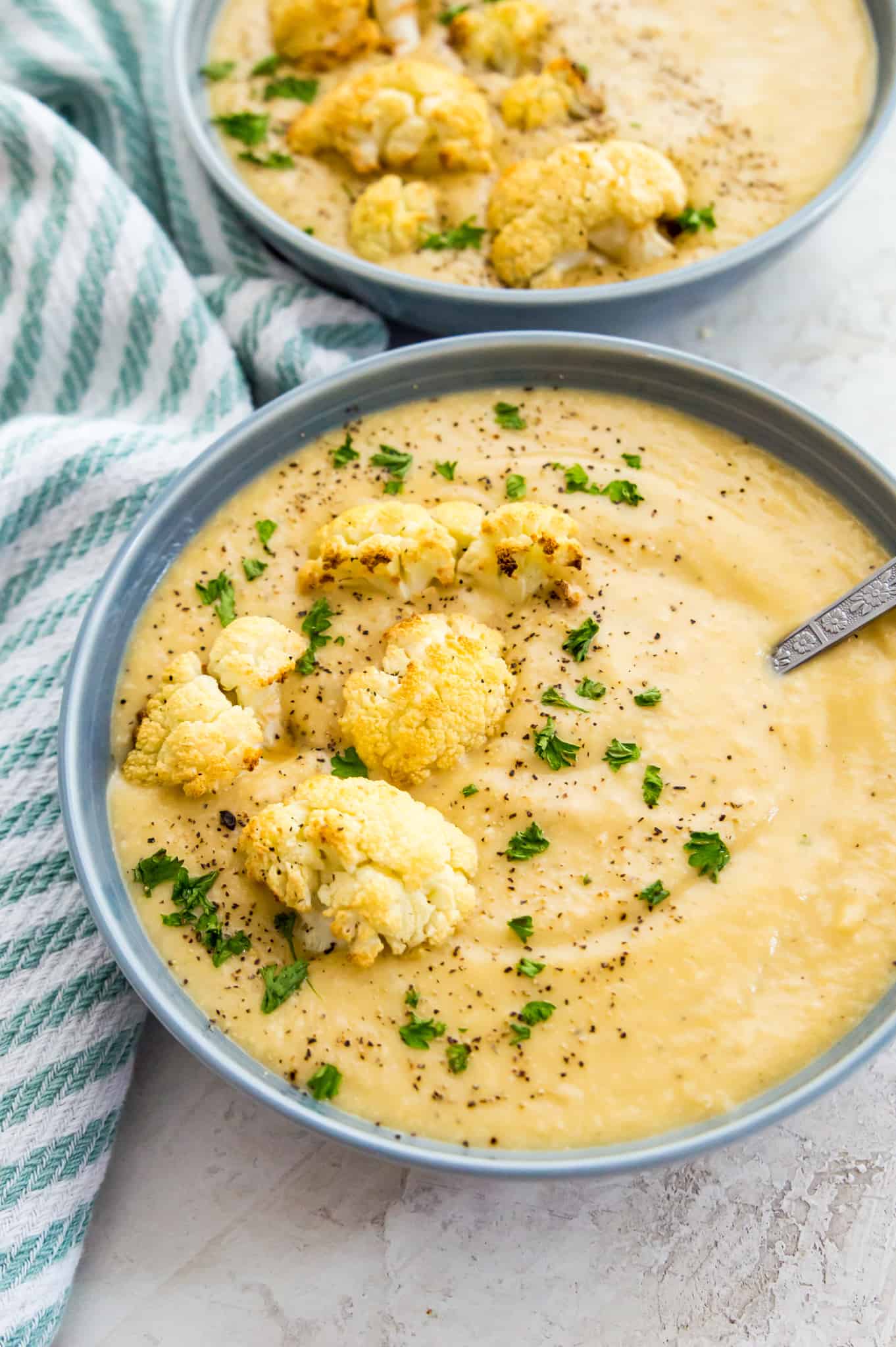 Bowls of creamy cauliflower soup topped with roasted cauliflower, black pepper and fresh parsley.