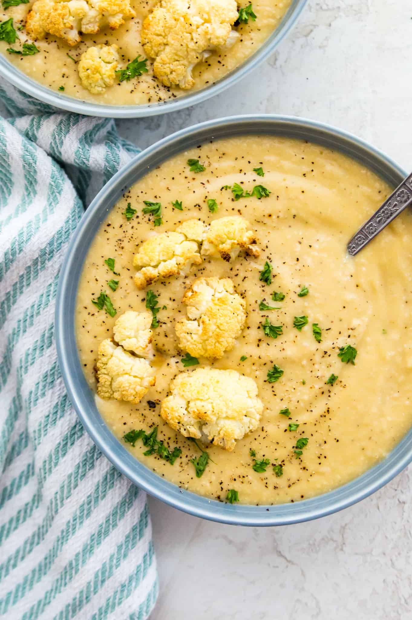 Bowls of cauliflower soup garnished with fresh parsley, roasted cauliflower and black pepper.