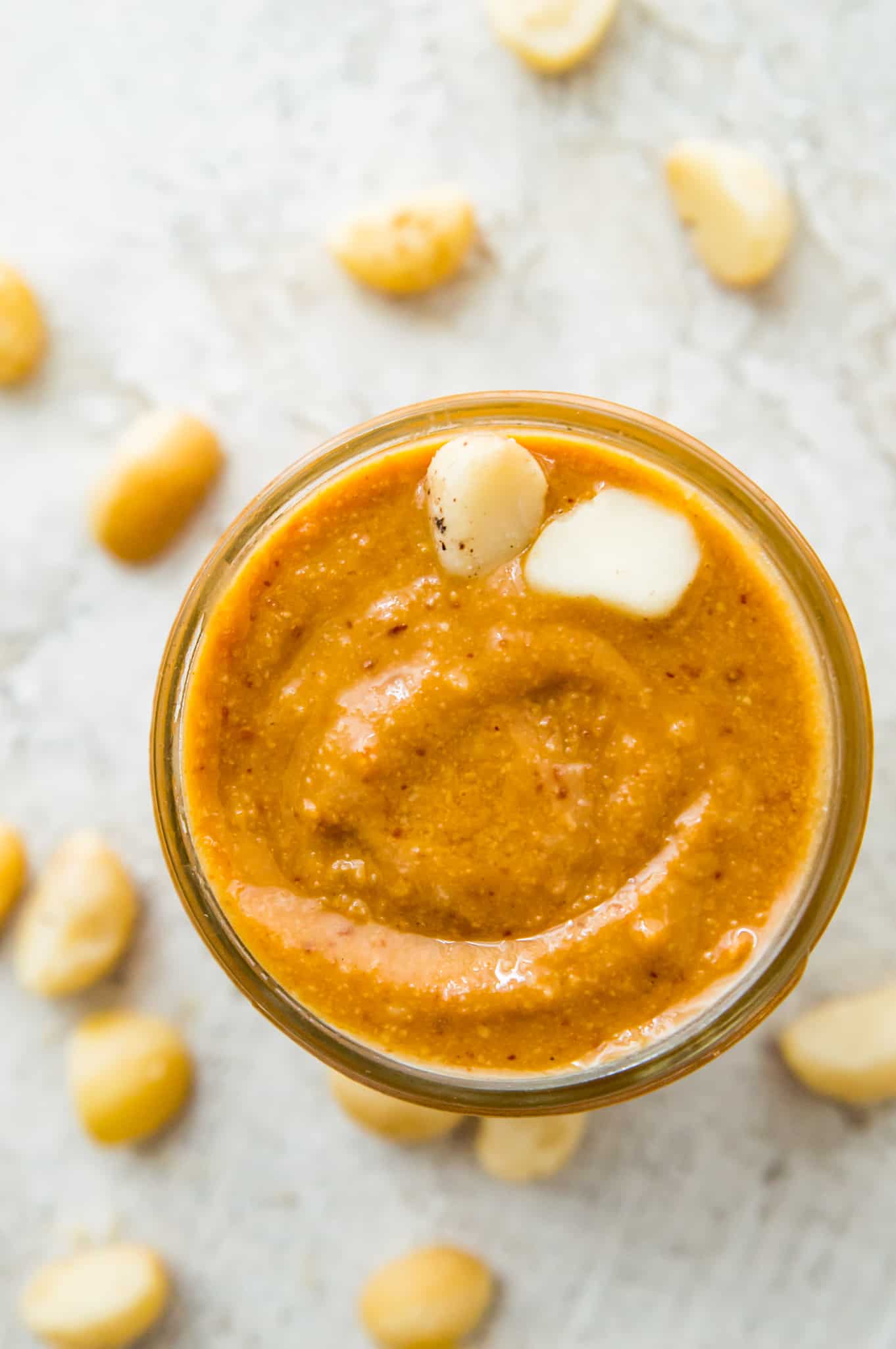 A jar of macadamia butter with two macadamia nuts on top.