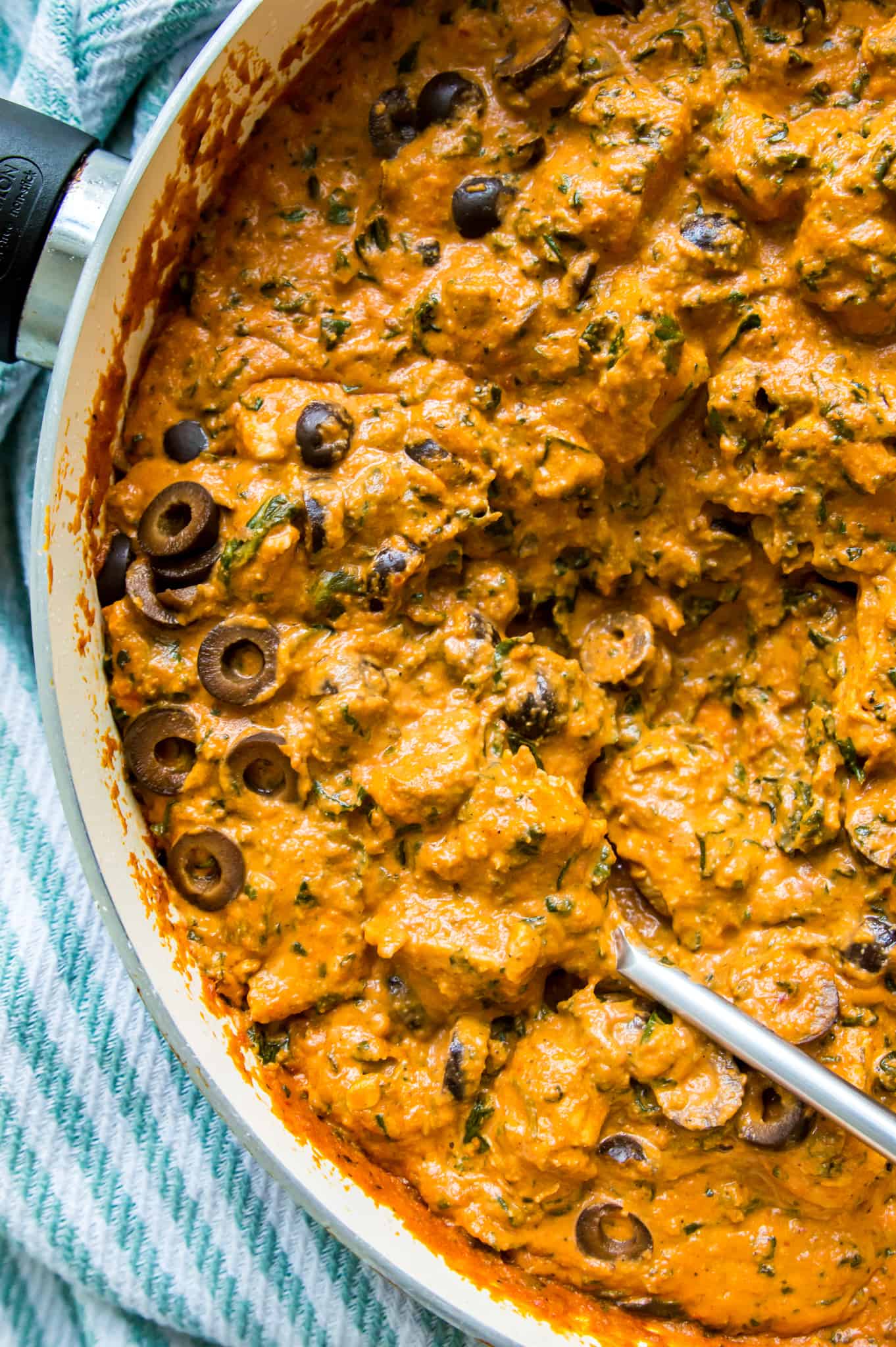 A pan full of a creamy Tuscan chicken and spinach recipe with a spoon in it.