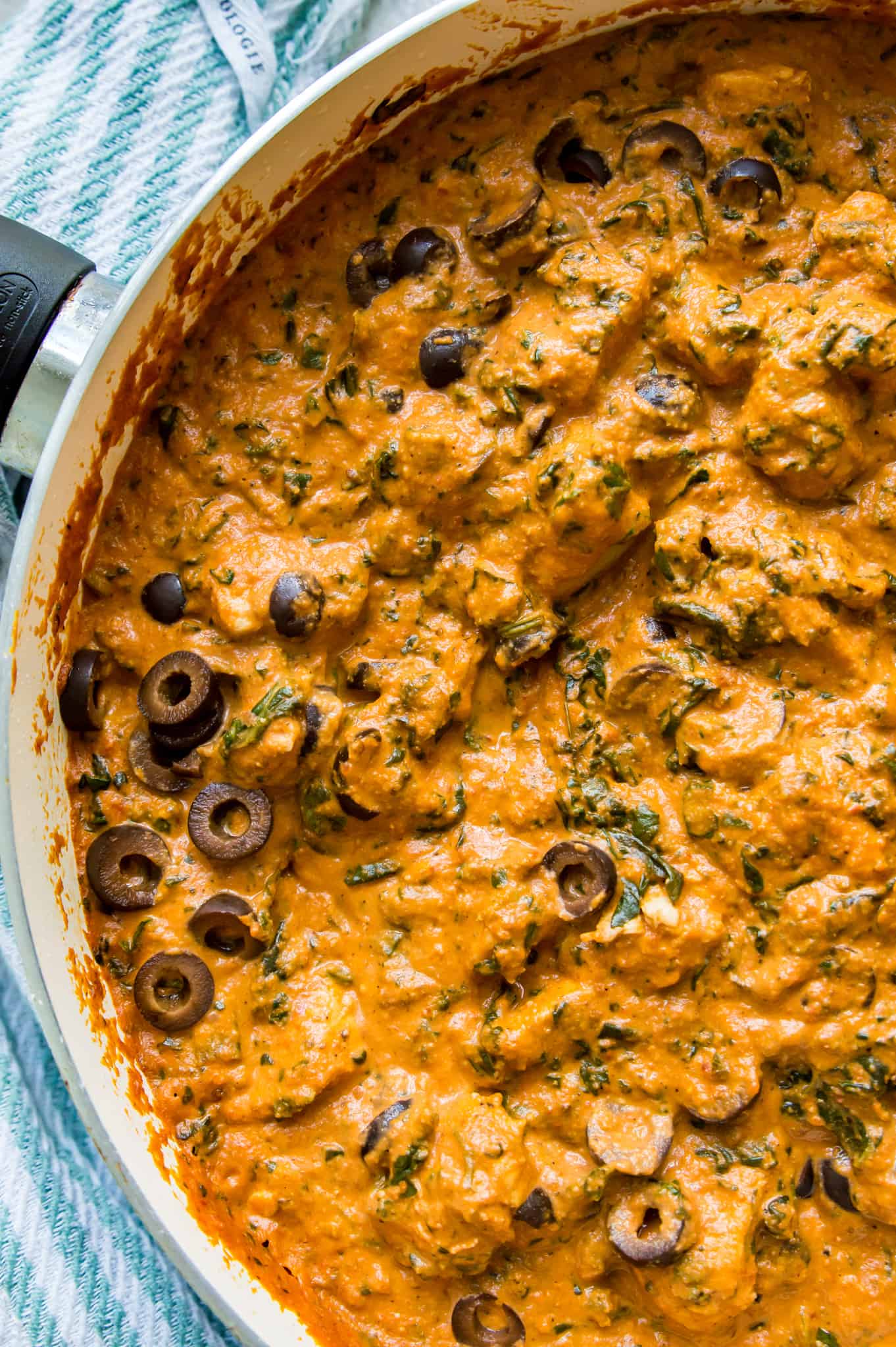 A pan of sun dried tomato chicken and spinach with a spoon in it.