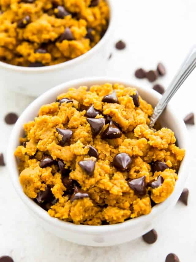 A bowl full of edible pumpkin cookie dough topped with and surrounded by chocolate chips.