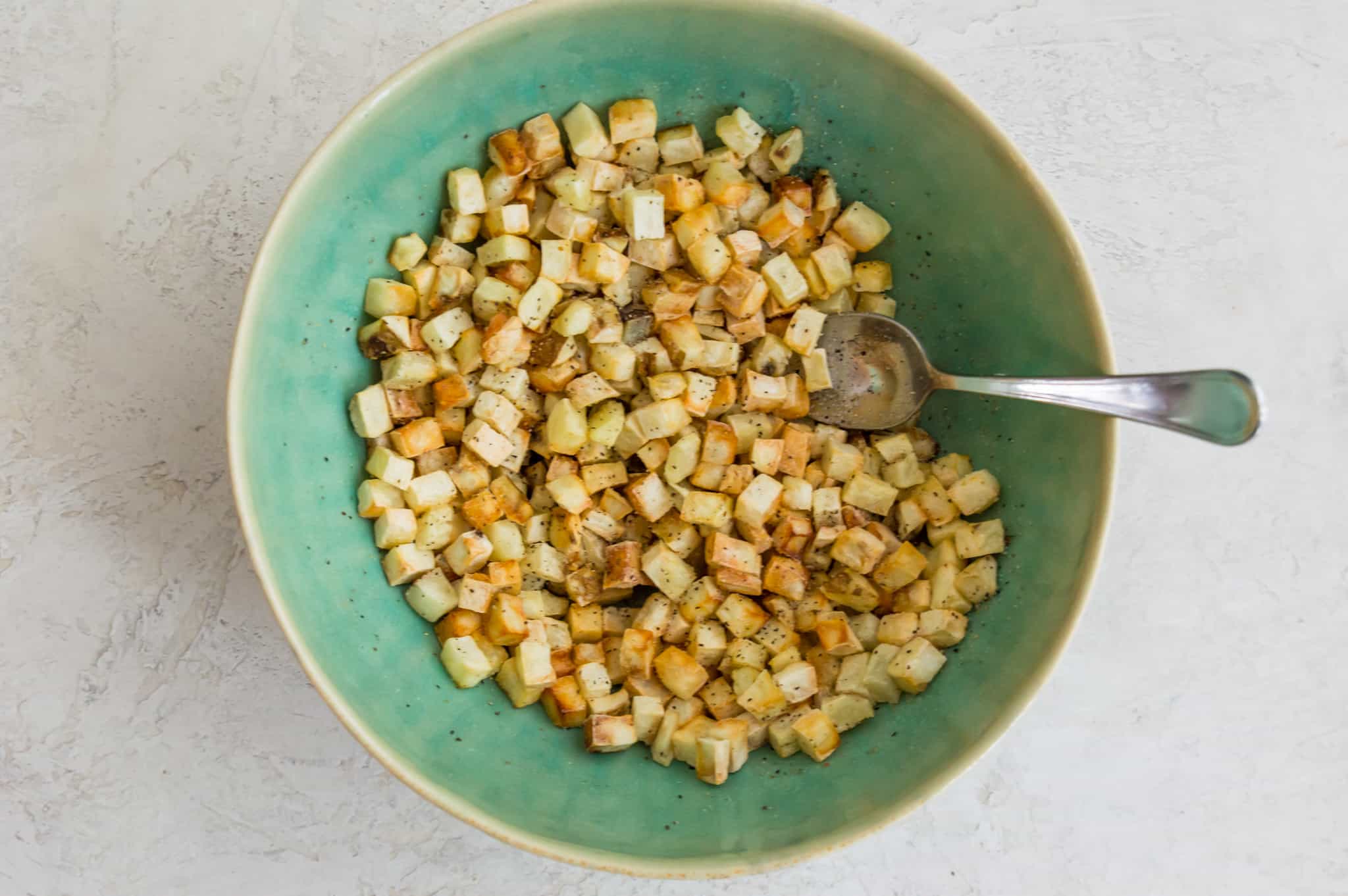 Cooked hash browns in a bowl with a spoon in it.