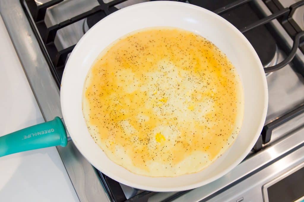 An egg omelette cooking on the stovetop in a pan.
