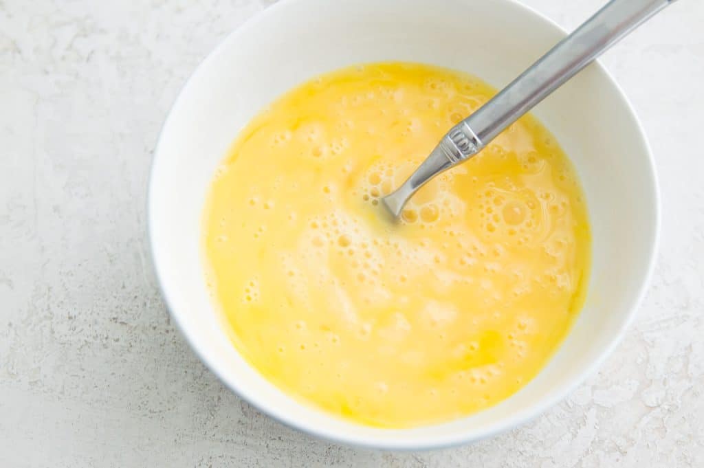 Whisked eggs in a bowl with a spoon in it.