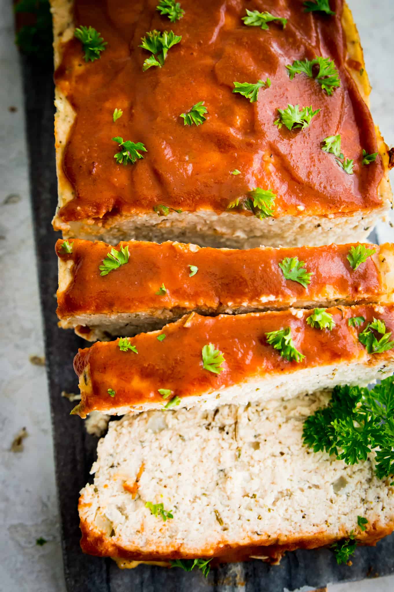 A chicken meatloaf cut up on a plate, garnished with fresh parsley.