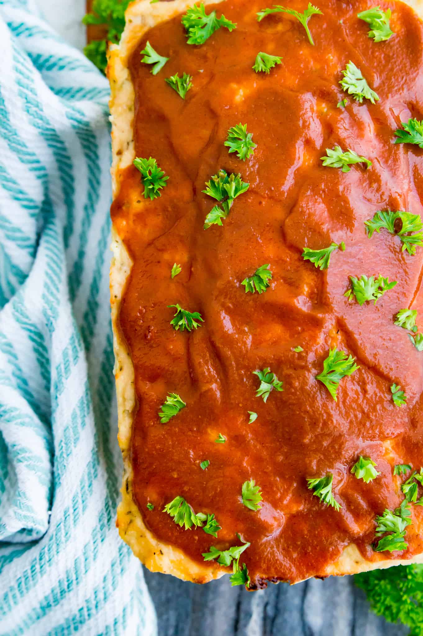 A loaf of chicken meatloaf topped with bbq sauce and fresh parsley.