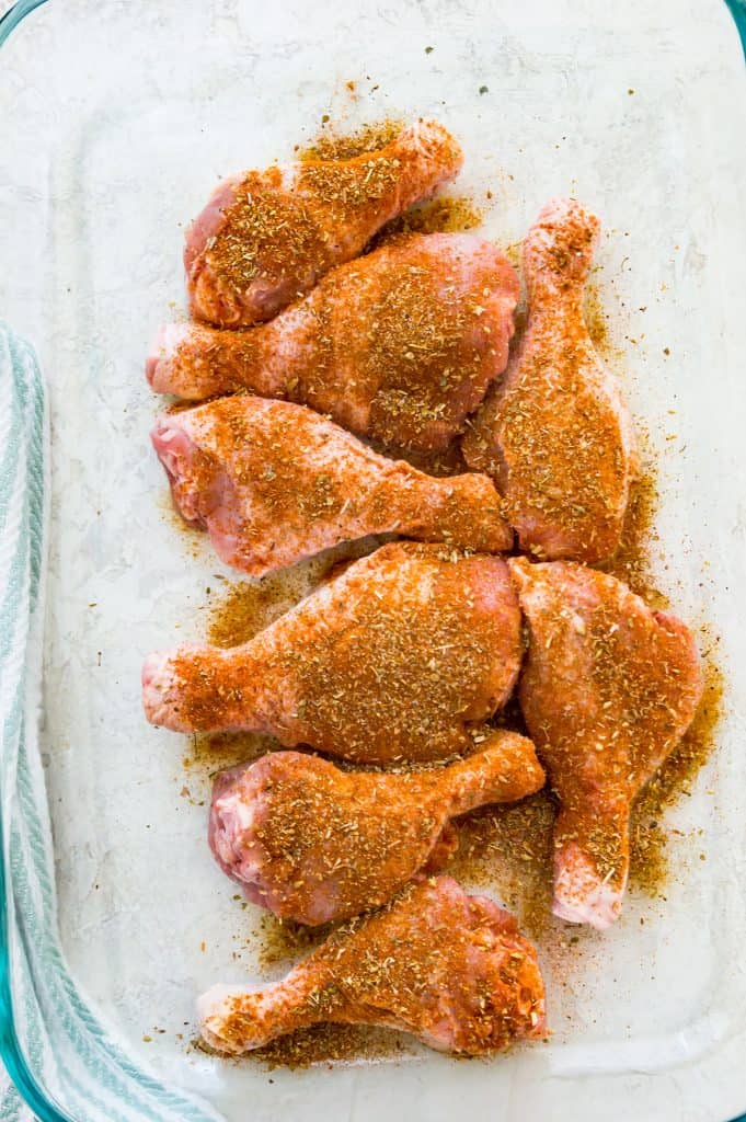 Chicken drumsticks coated in a spice rub in a glass baking dish.