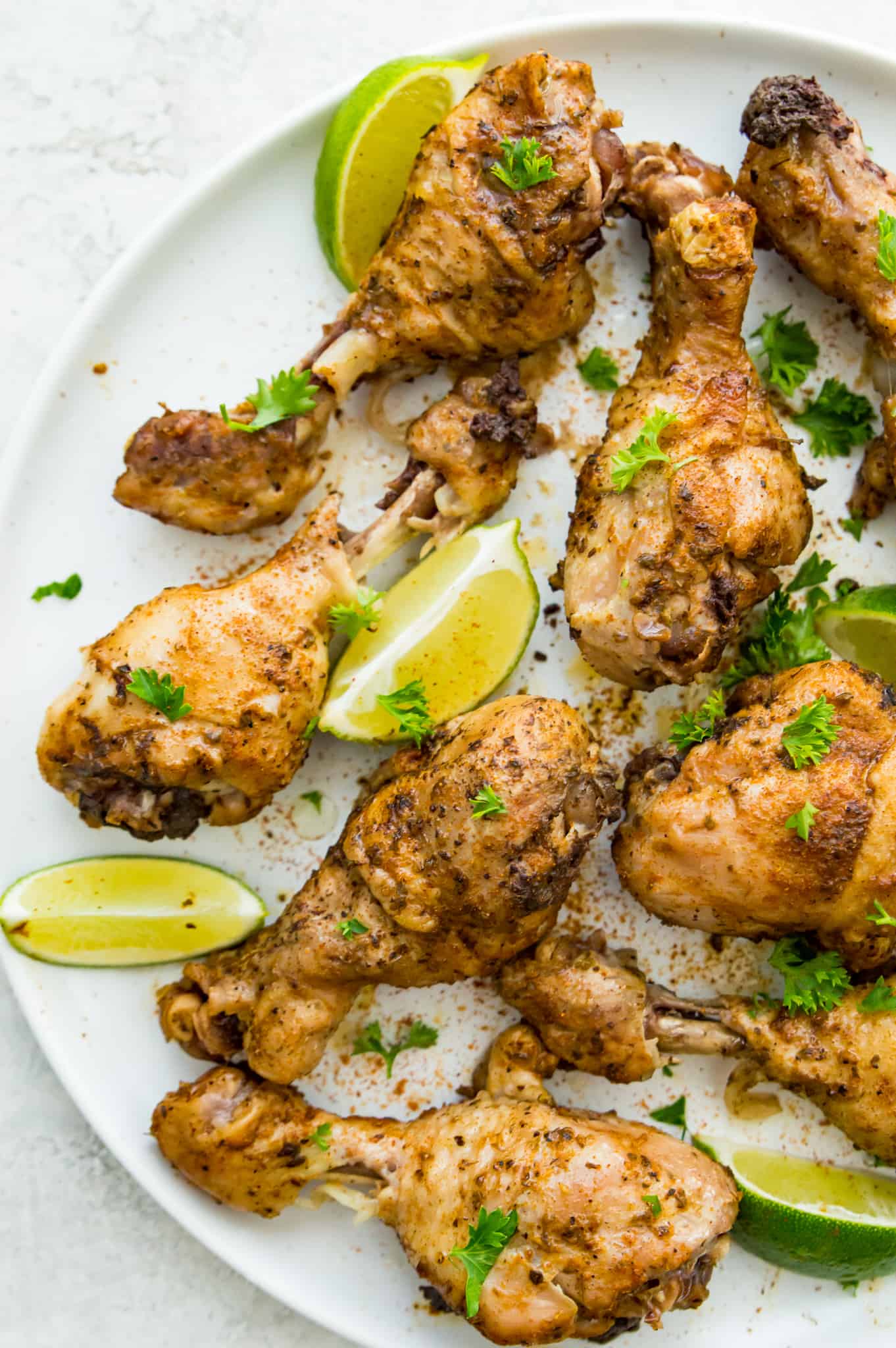 A plate of cooked chicken drumsticks garnished with cilantro with lime wedges beside them.
