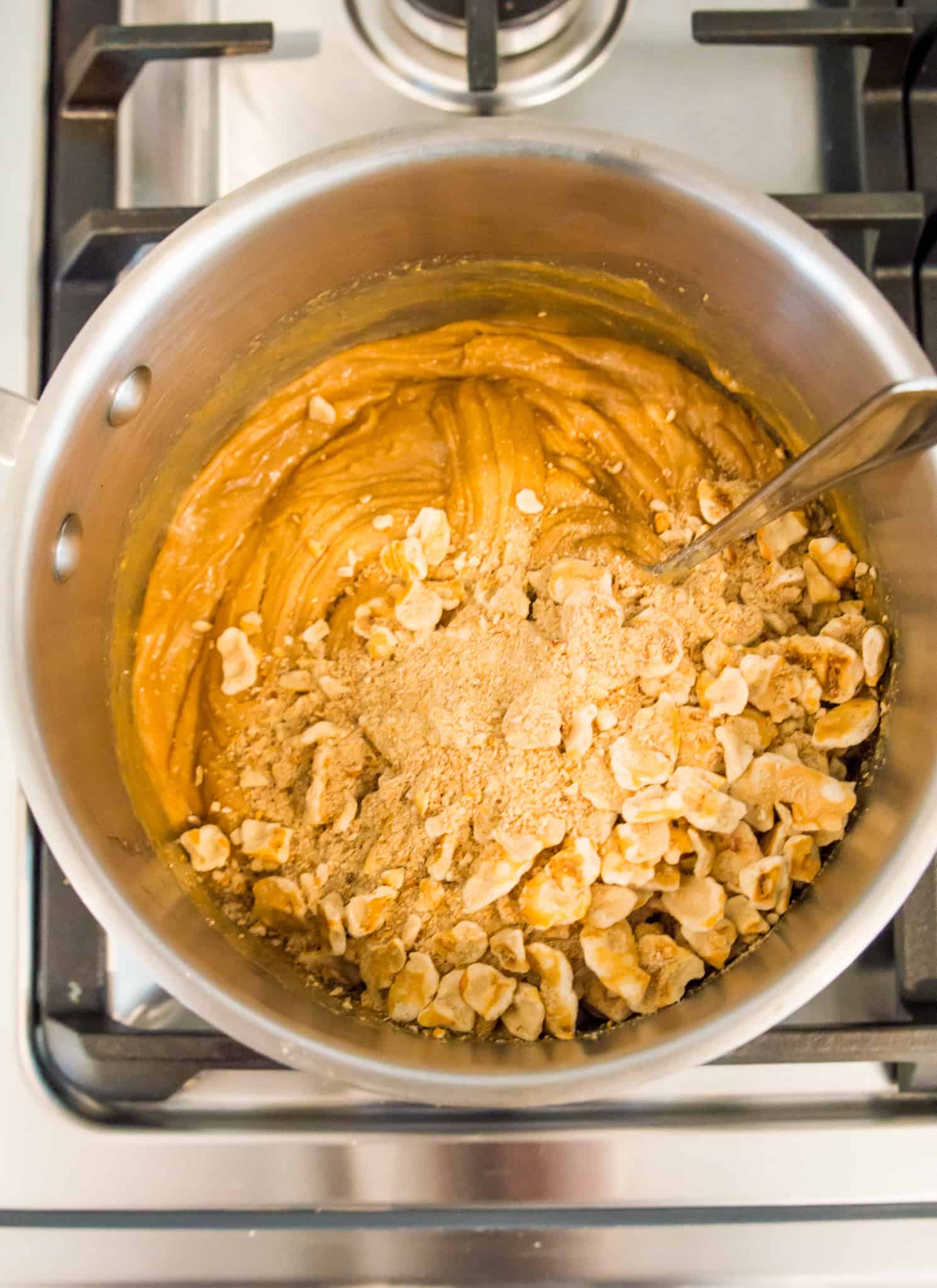 A pot on the stove with peanut butter and pretzel pieces. 
