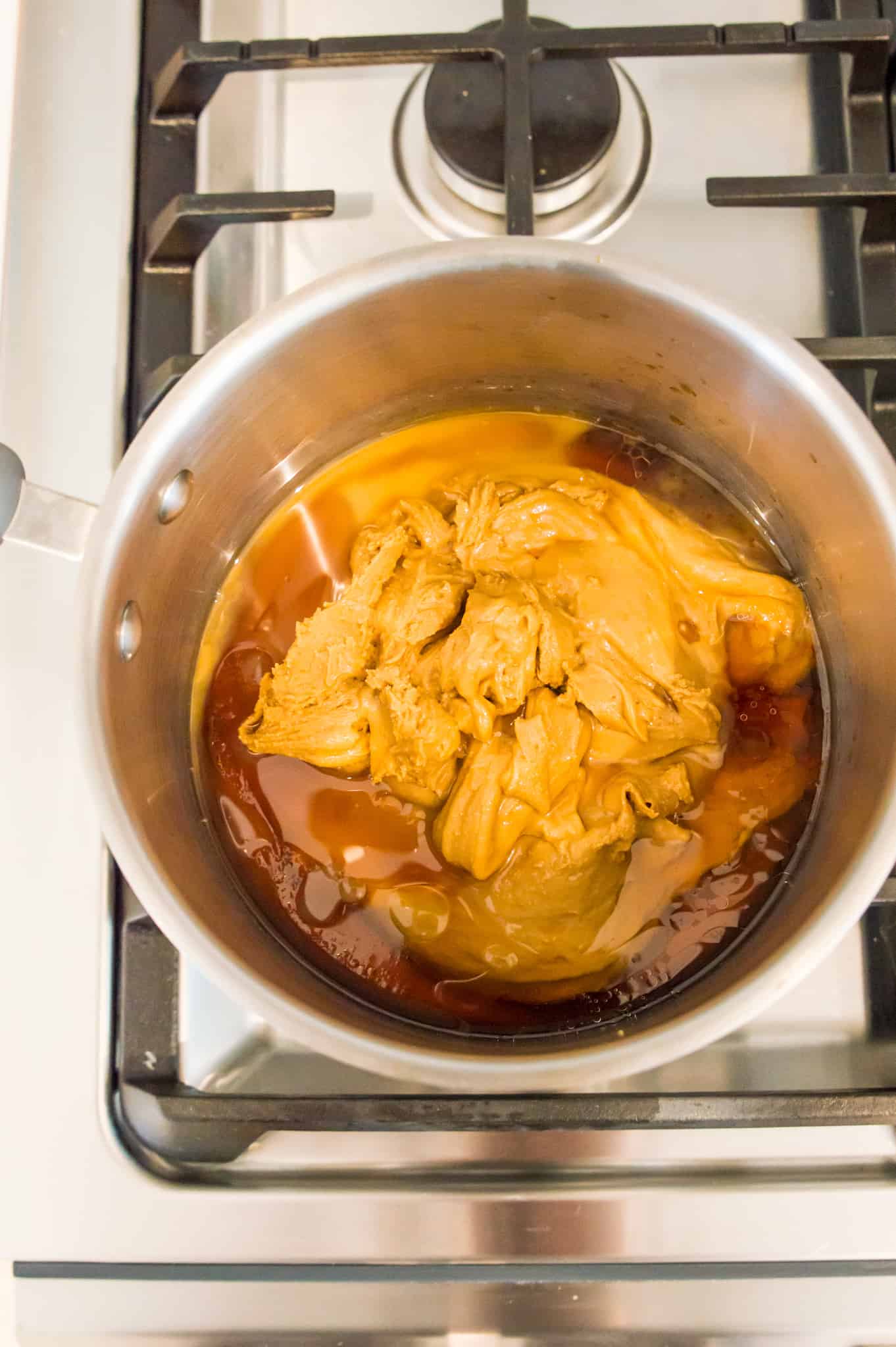 A pot on the stovetop with peanut butter and maple syrup in it.