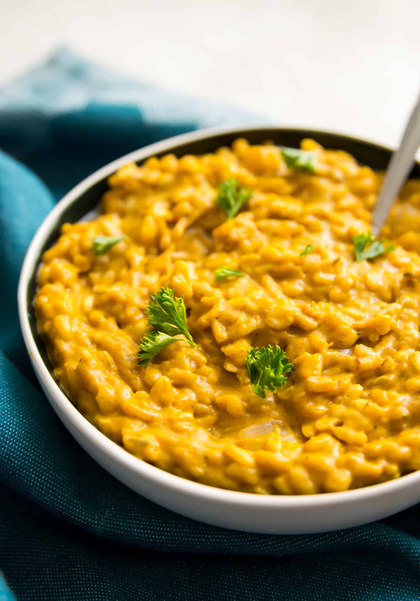 A bowl of pumpkin risotto with a spoon in it and fresh parsley as garnish.