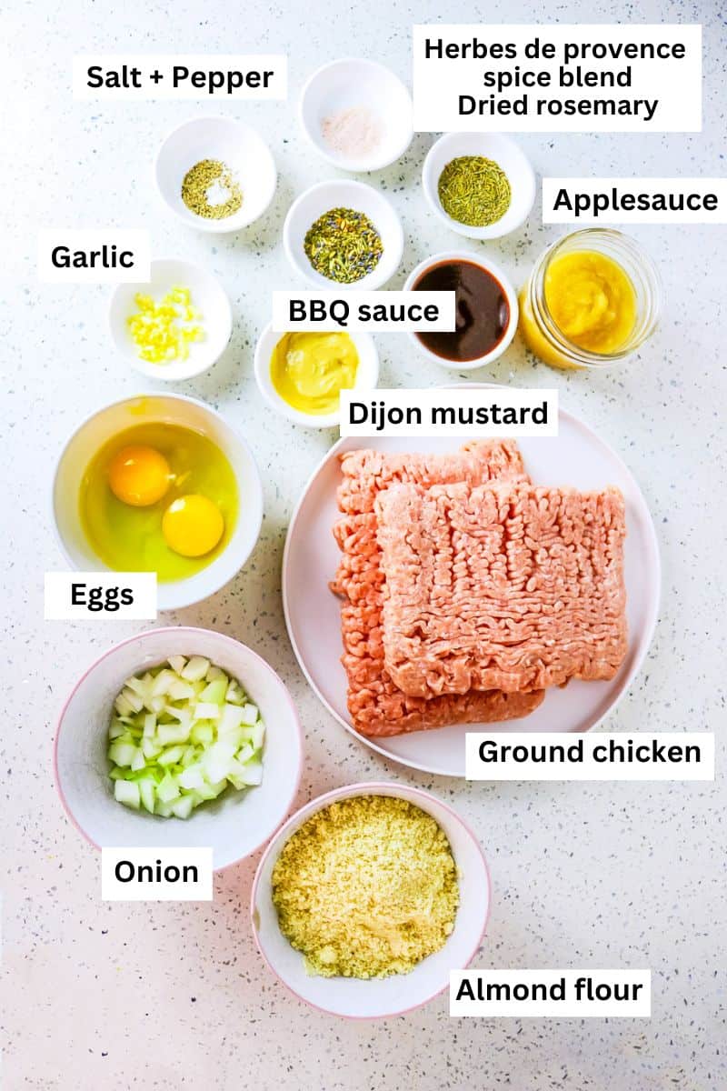 Ingredients for making chicken meatloaf separated into bowls including ground chicken, applesauce, mustard, spices, eggs and almond flour.