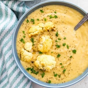 A bowl of creamy cauliflower soup topped with roasted cauliflower and fresh parsley.