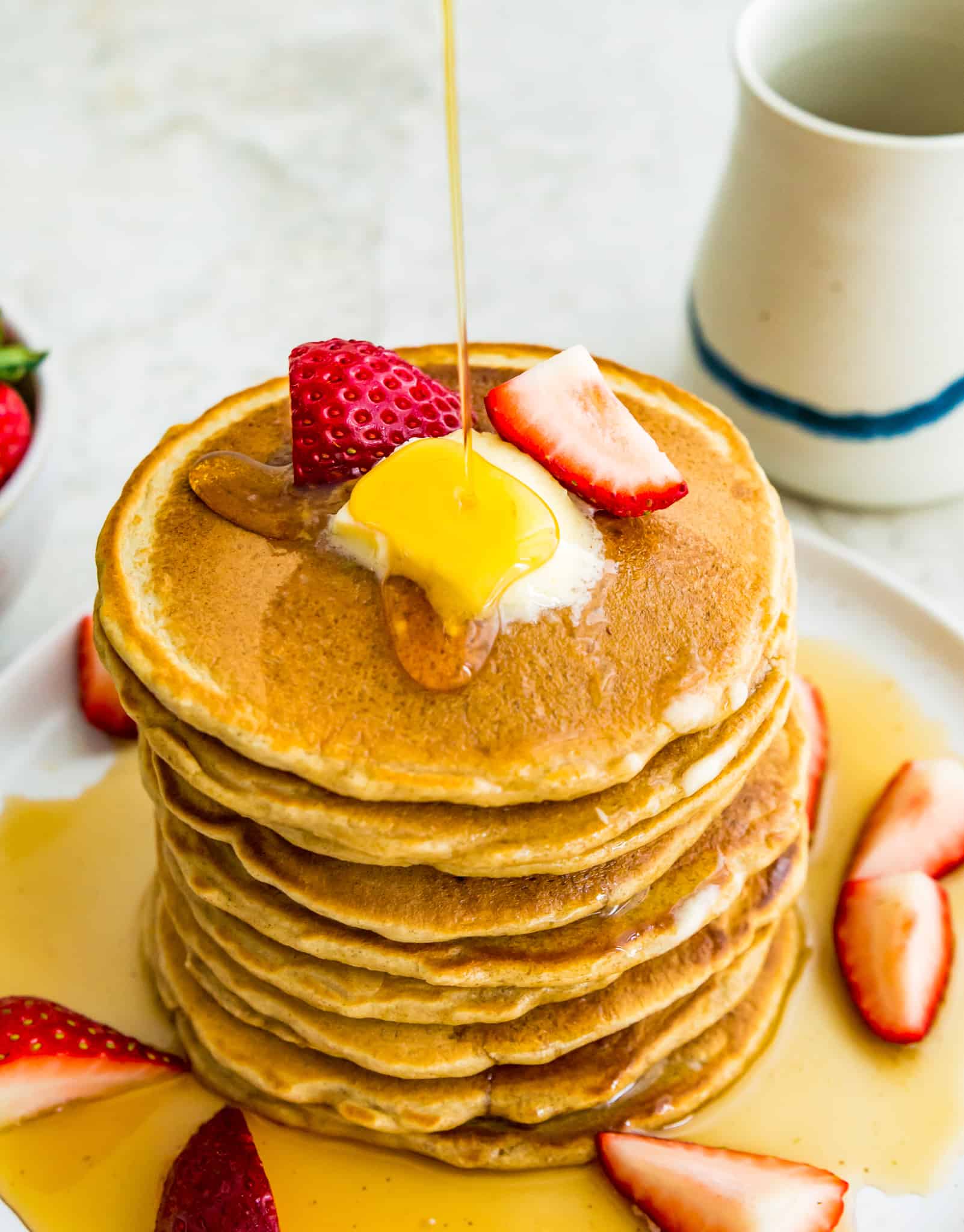A stack of oat flour pancakes with butter and strawberries on top.