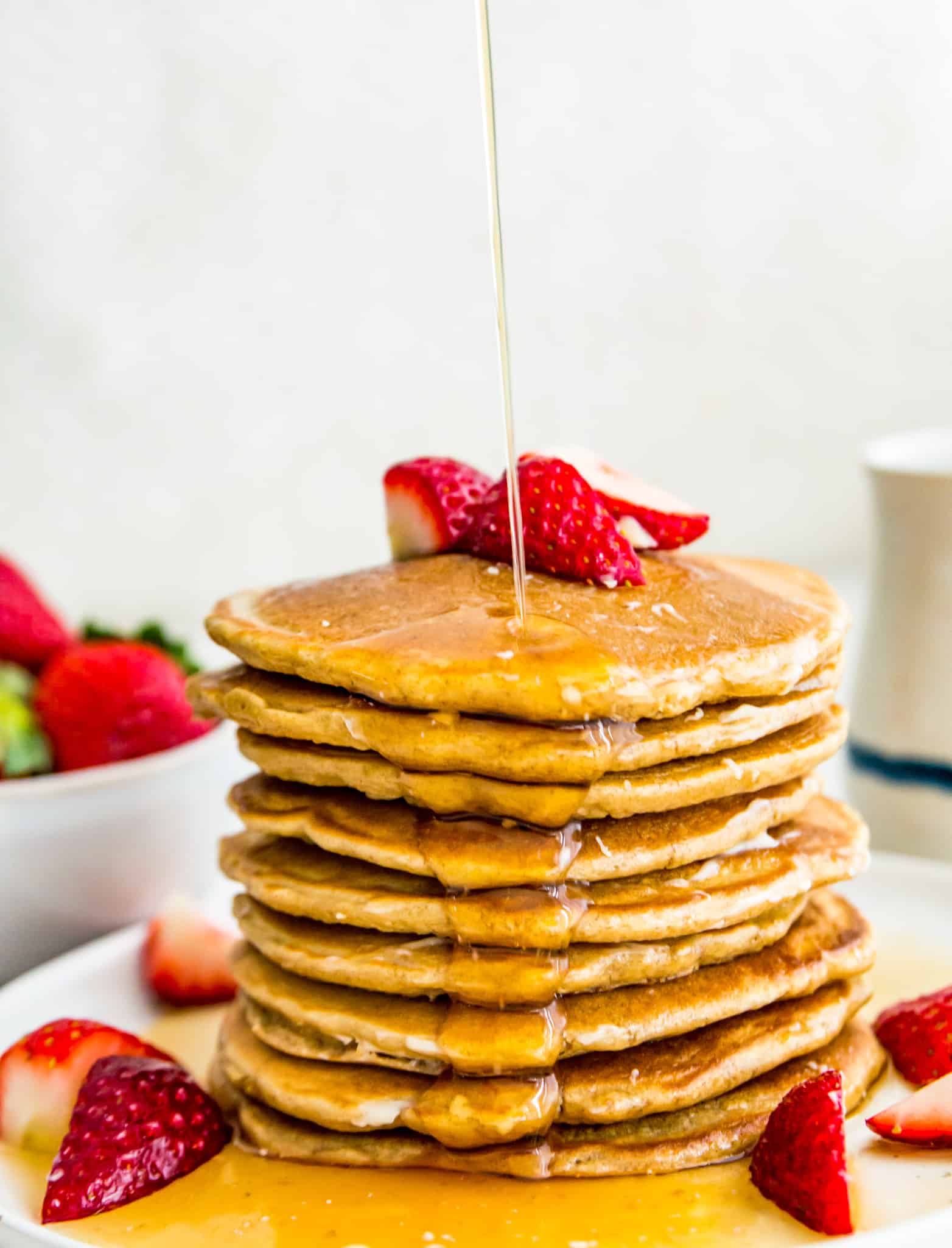 A stack of oat flour pancakes with syrup being poured on them.