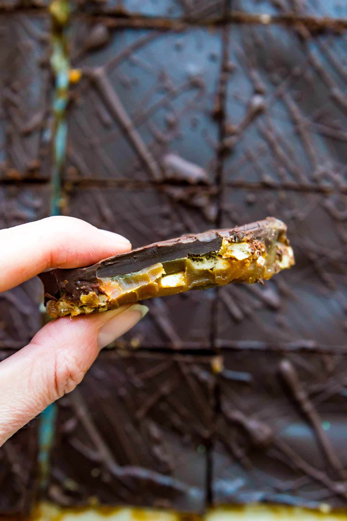 A hand holding a piece of chocolate toffee pretzel bar.