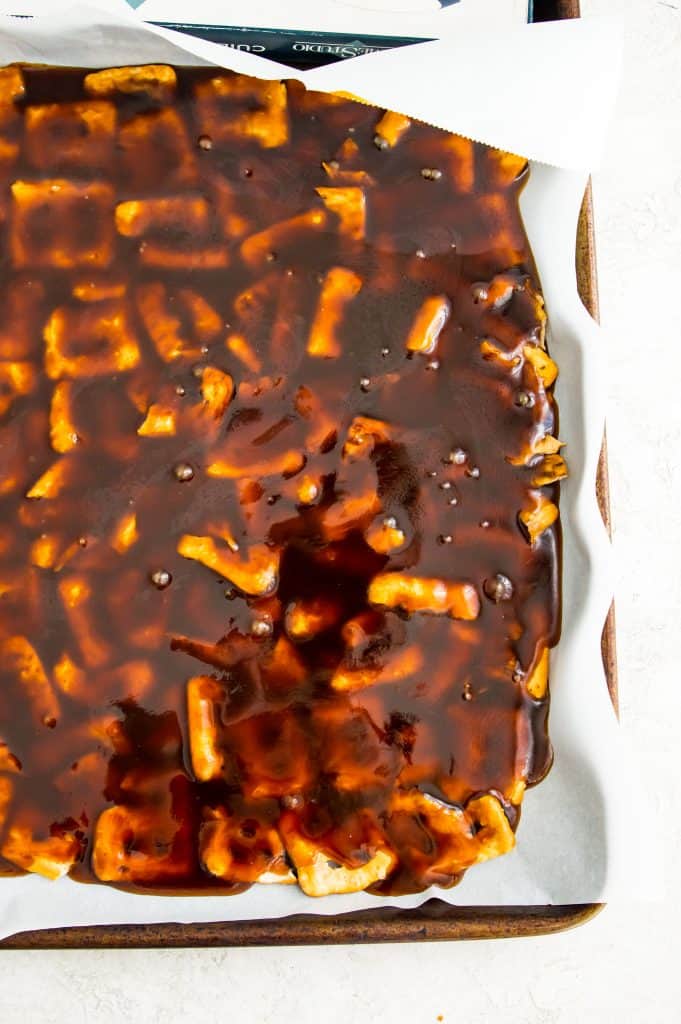 Caramel sauce poured over pretzels on a baking sheet.