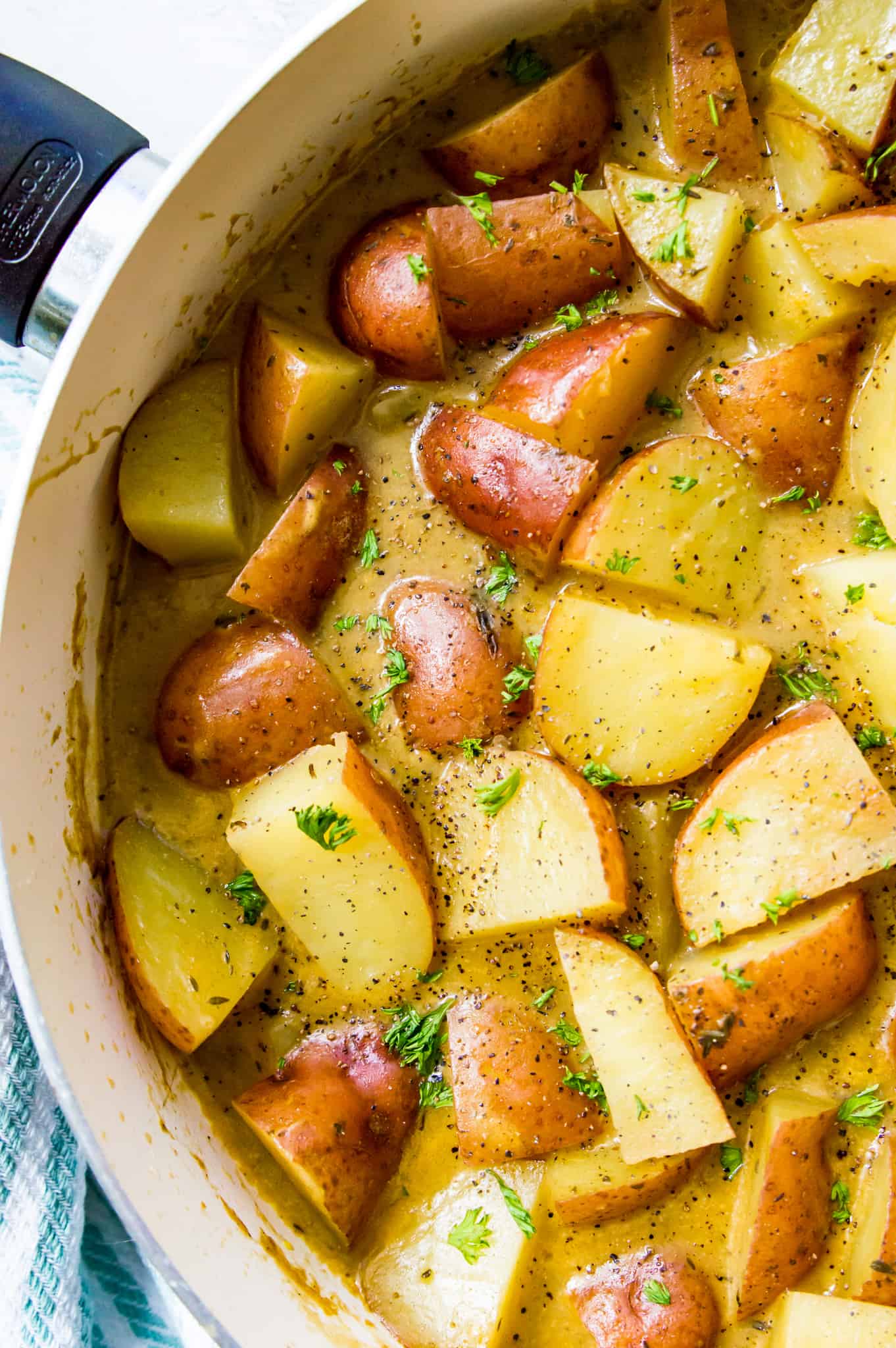 A pan full of stewed potatoes topped with fresh herbs.
