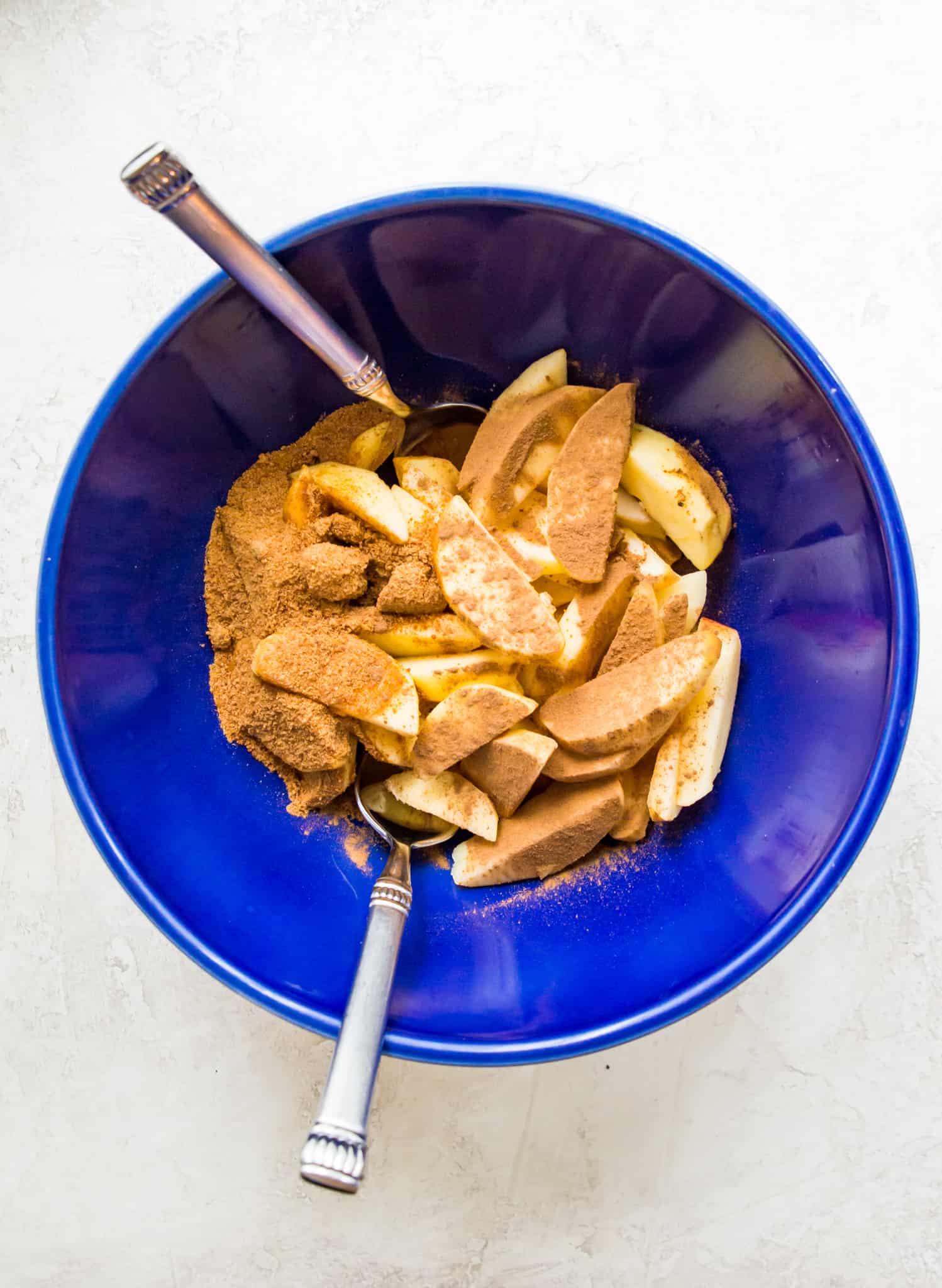 A bowl of peeled and chopped apples coated in a cinnamon sugar mixture.