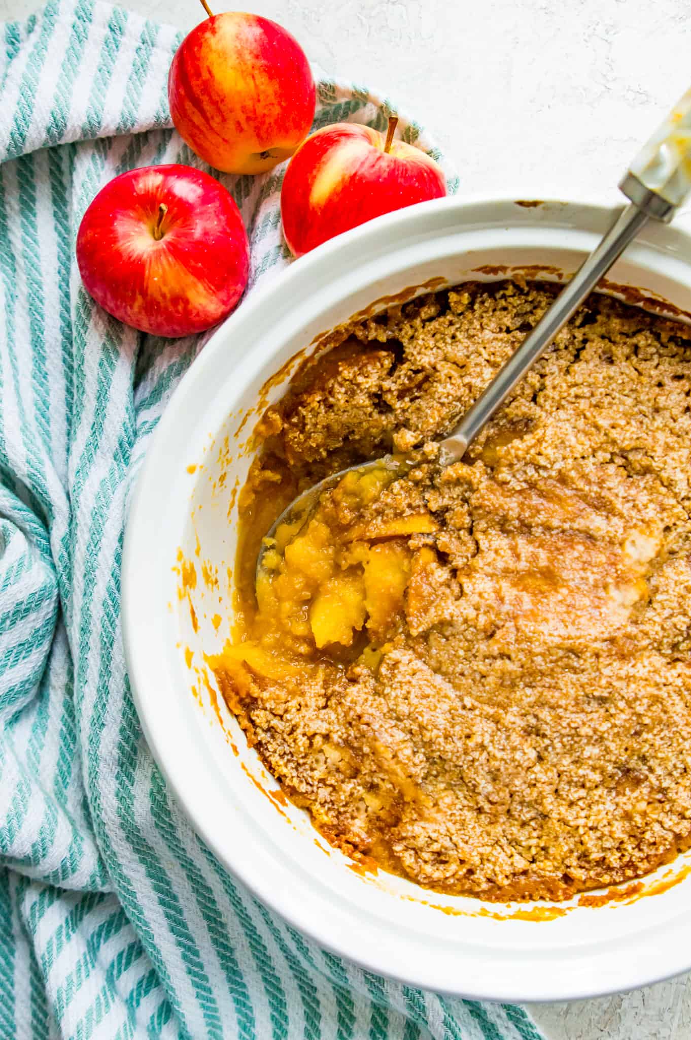 A white casserole dish filled with turnip apple casserole with a large serving spoon in it.