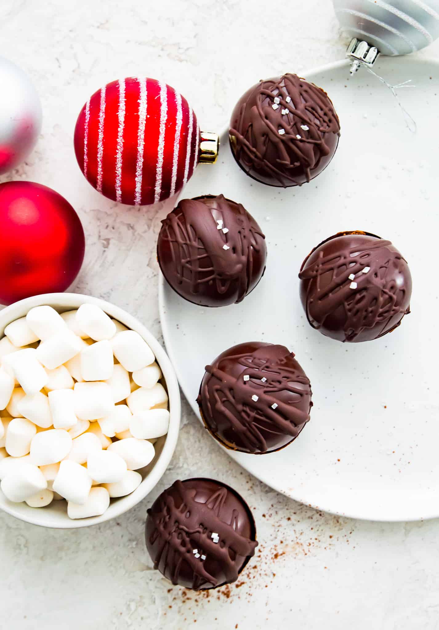 Dairy-free hot chocolate bombs on a plate with a bowl of marshmallows beside them.
