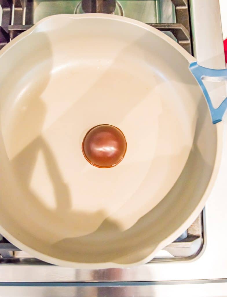Half a chocolate sphere being heated in a frying pan on the stovetop.