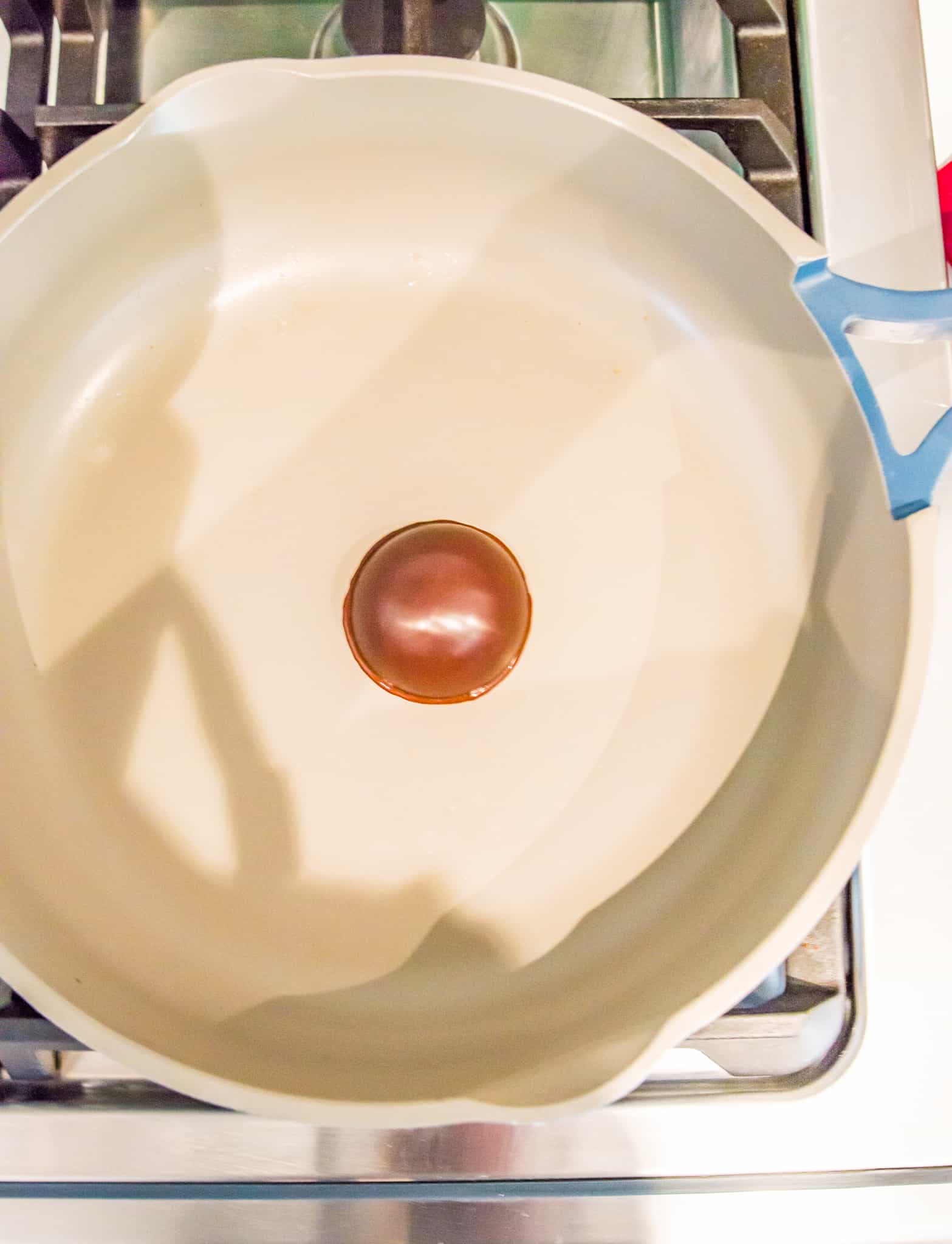 Half a chocolate sphere being heated in a frying pan on the stovetop.