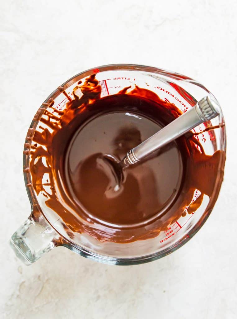 A glass measuring cup full of melted chocolate with a spoon in it.