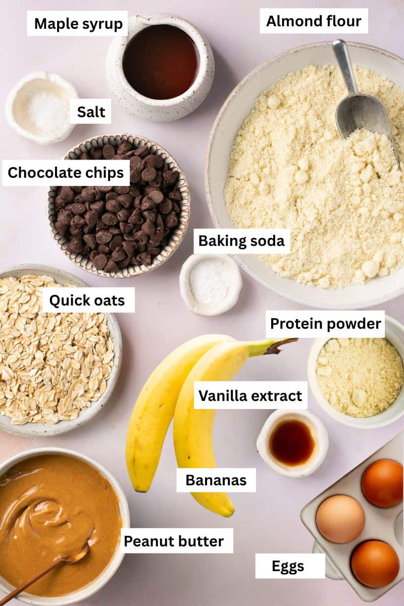 The ingredients for making banana protein muffins separated in bowls including flour, oats, bananas, eggs, chocolate chips, protein powder and peanut butter.