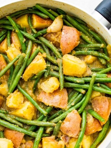 A pan filled with cooked green beans and potatoes.