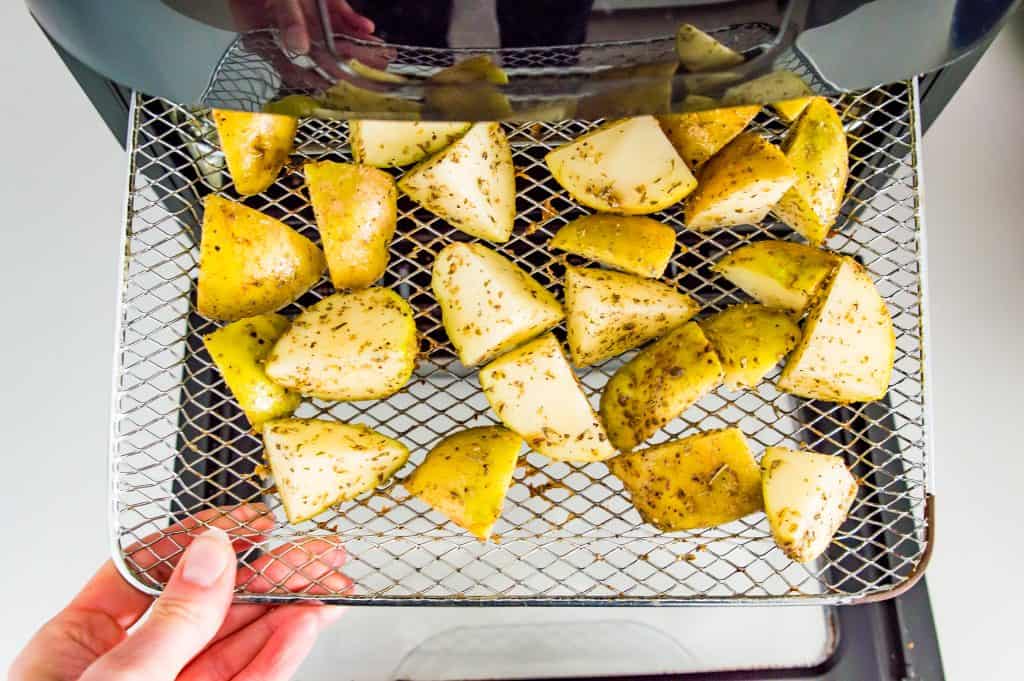 Seasoned, diced potatoes on the rack of an air fryer.