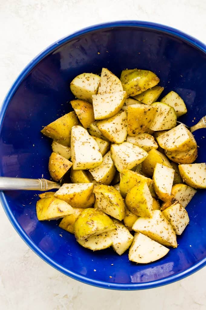 A bowl filled with diced potatoes topped with spices and with a spoon in the bowl.