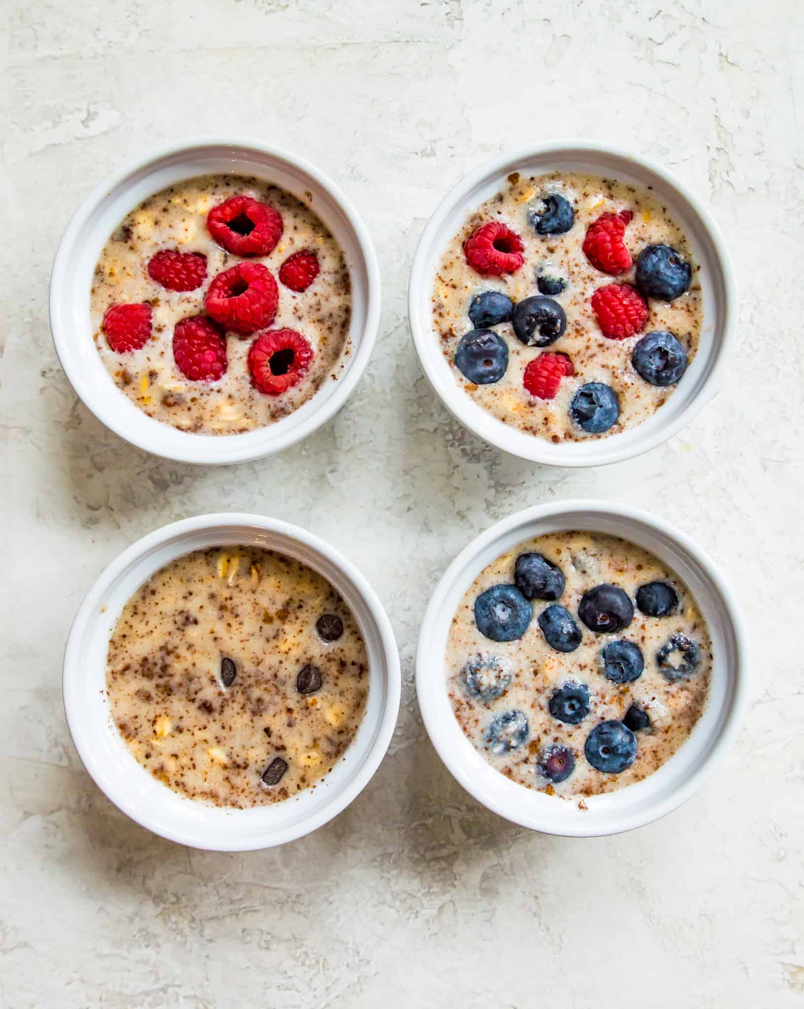 Four ramekins filled with oats and topped with fresh blueberries and raspberries.