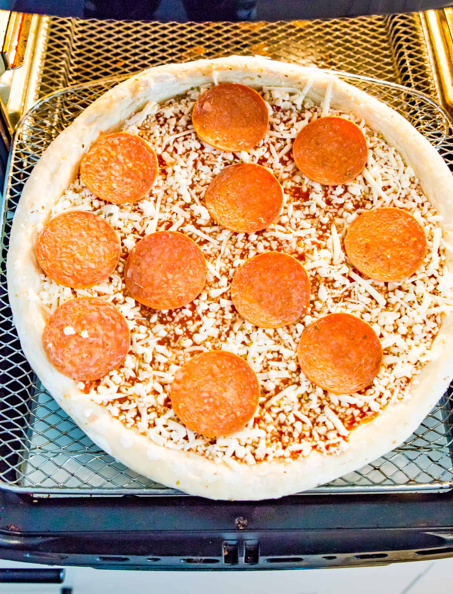 A frozen pepperoni pizza on an air fryer tray.