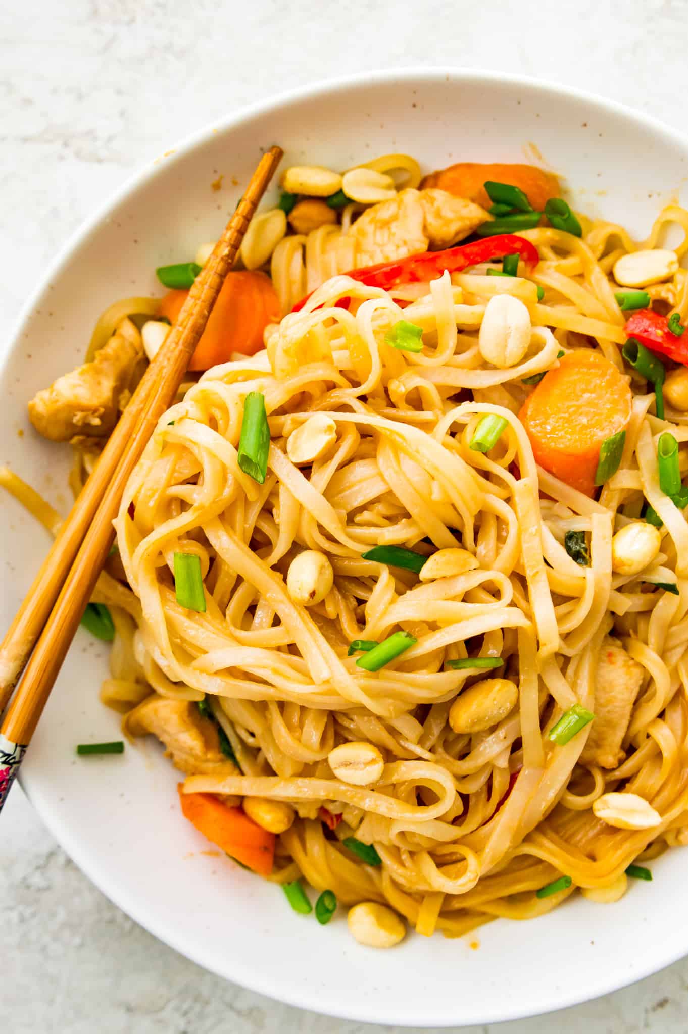 A bowl of pad thai with chicken and vegetables topped with peanuts 