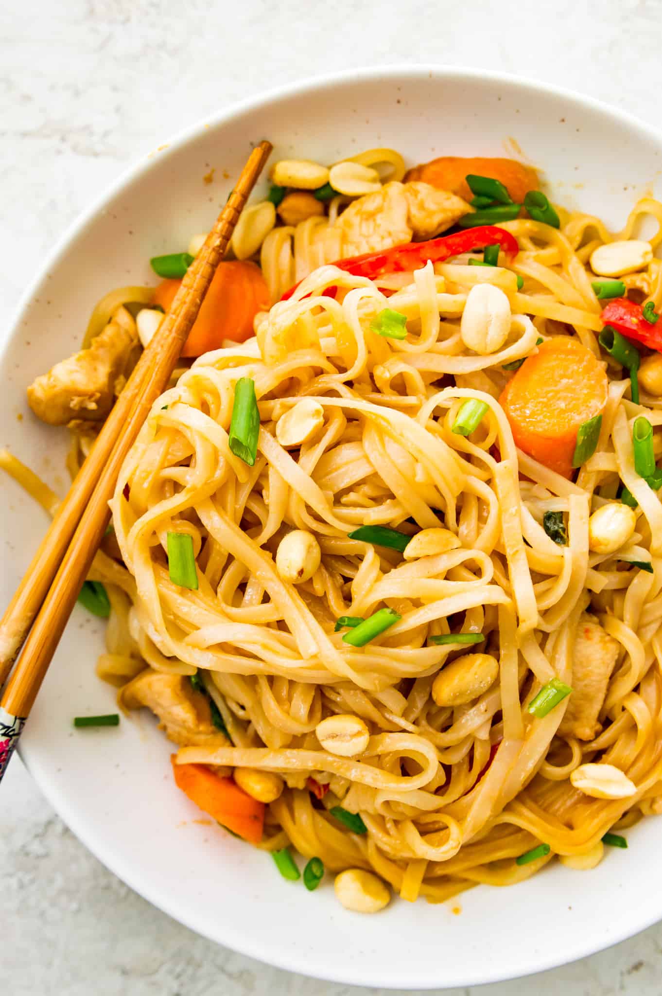 A bowl of pad Thai with chicken and vegetables topped with peanuts.