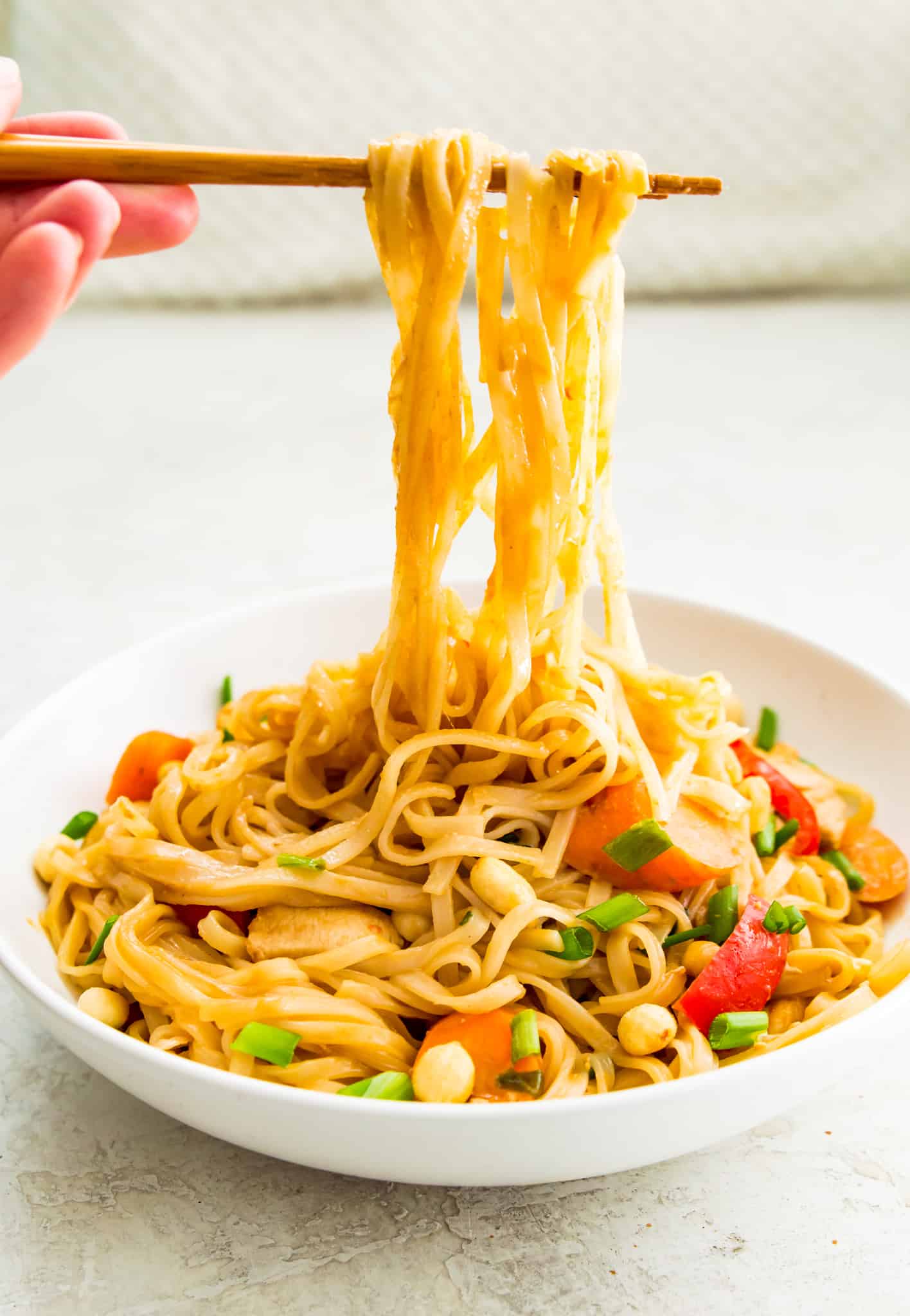 A bowl of chicken pad Thai with chop sticks pulling noodles out of the bowl.