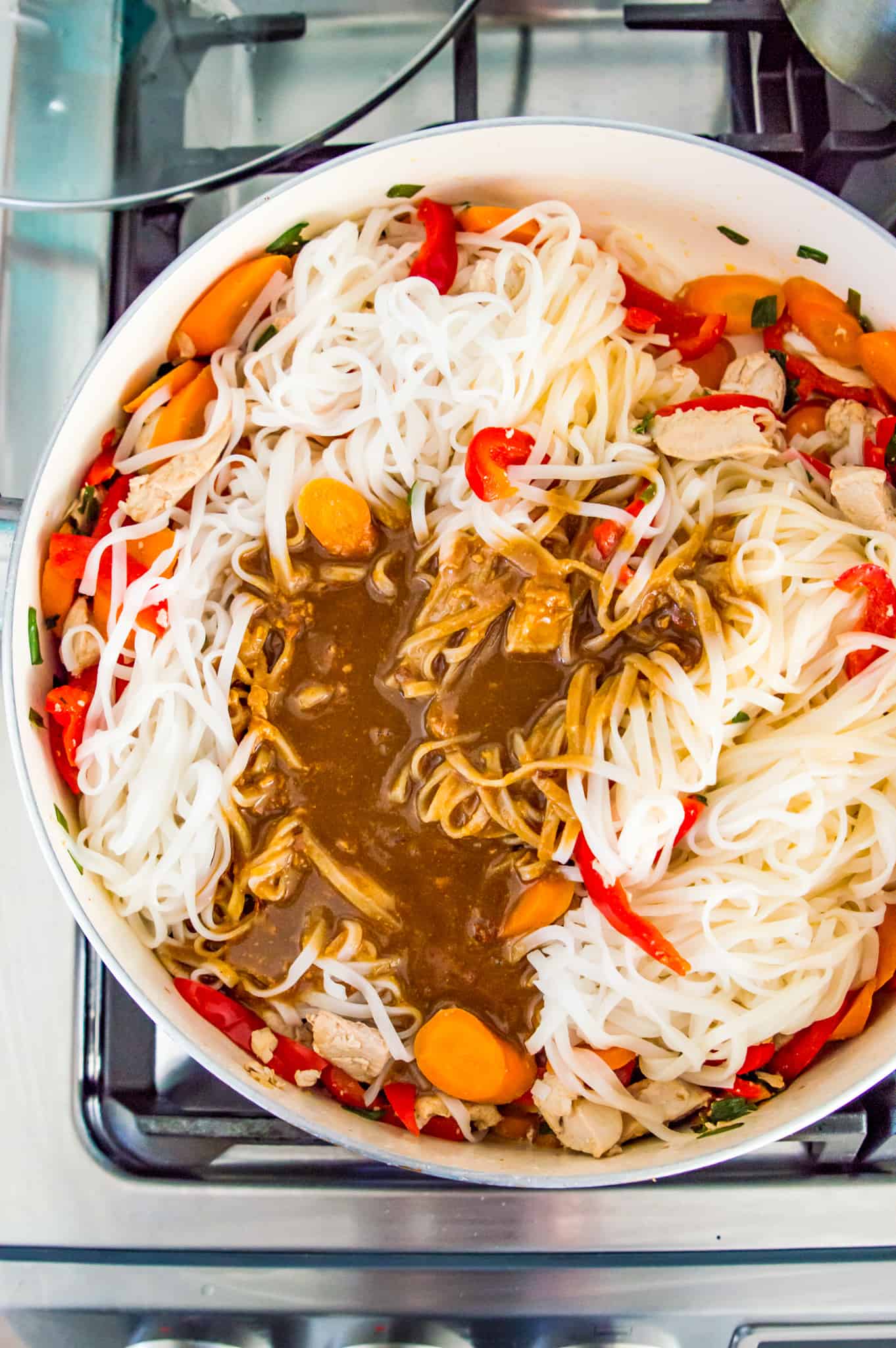 A pan with rice noodles, sauce and chopped vegetables in it.