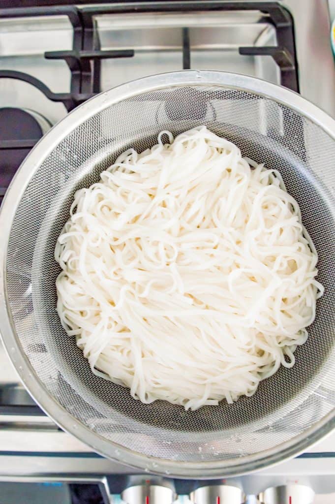 A colander filled with cooked rice noodles.