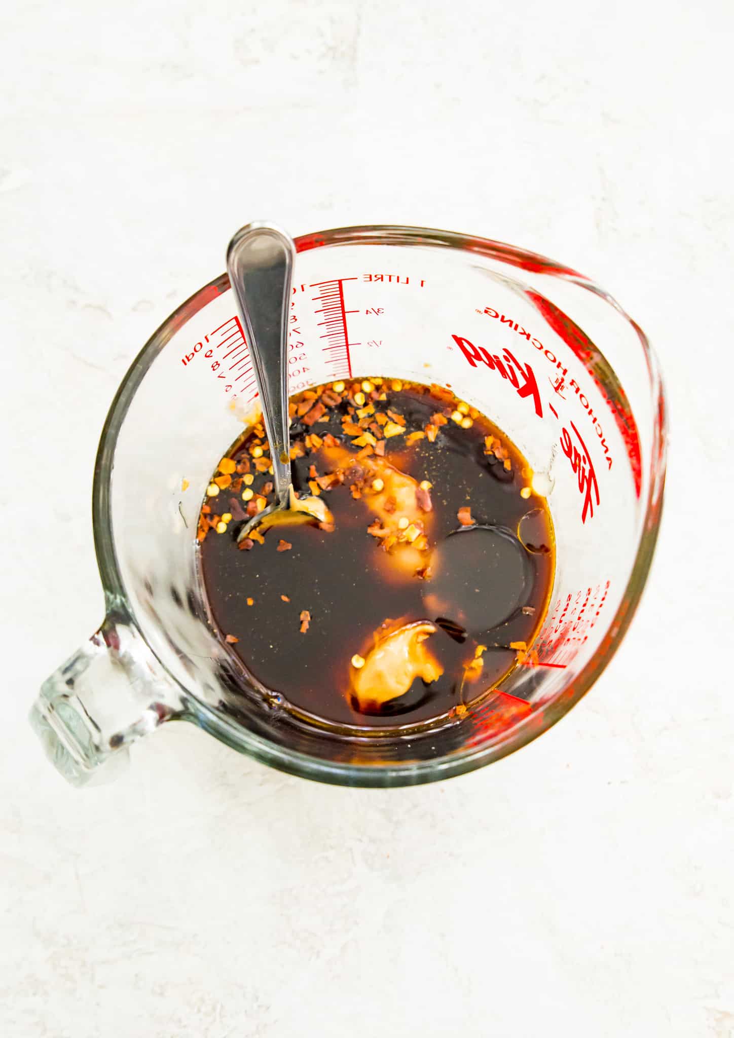 A glass measuring cup with soy sauce, peanut butter, chili flakes and honey in it.