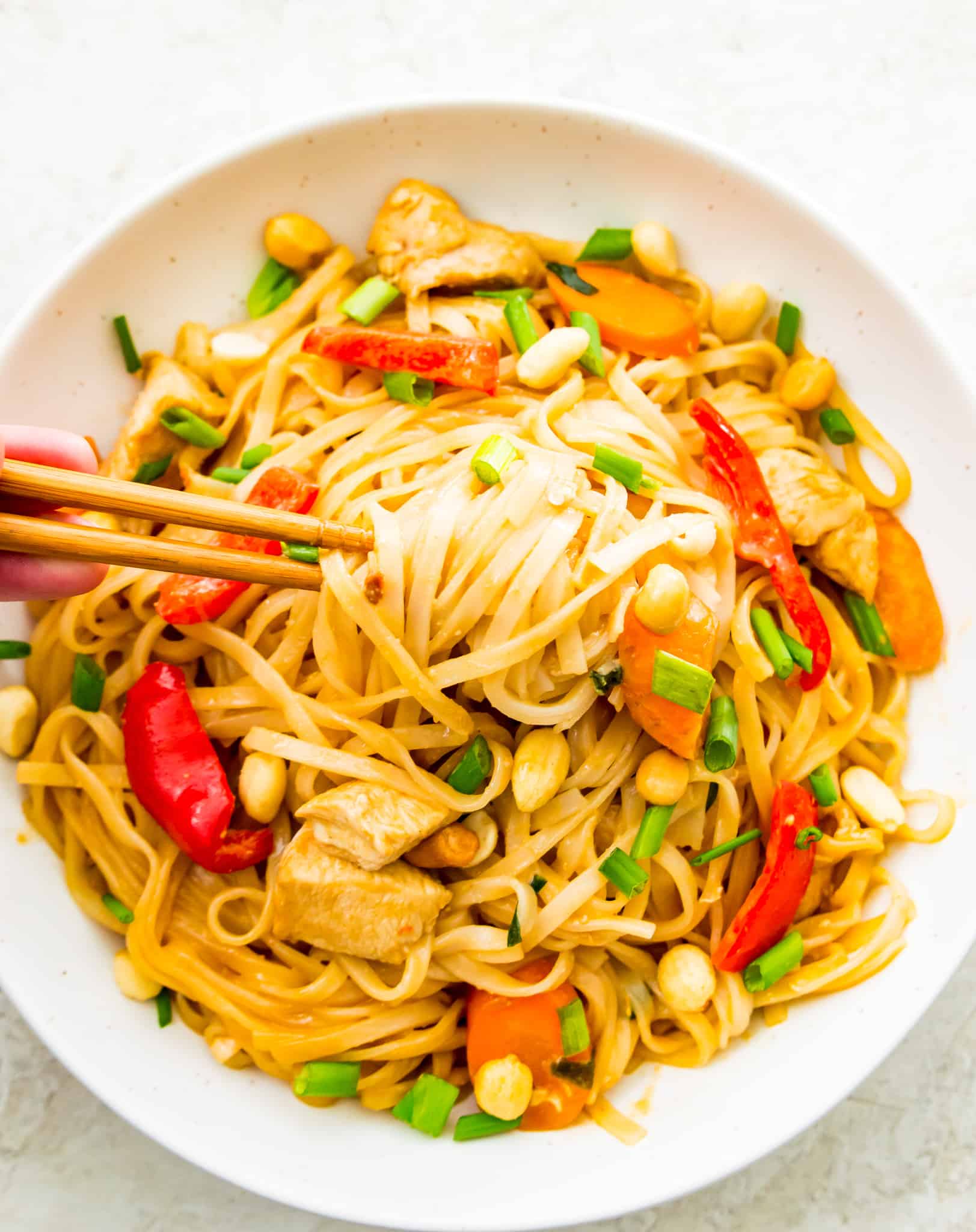 A bowl of gluten free pad Thai with chicken, vegetables and peanuts in it.
