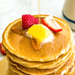 A stack of oat flour pancakes with butter on top and syrup being poured on it