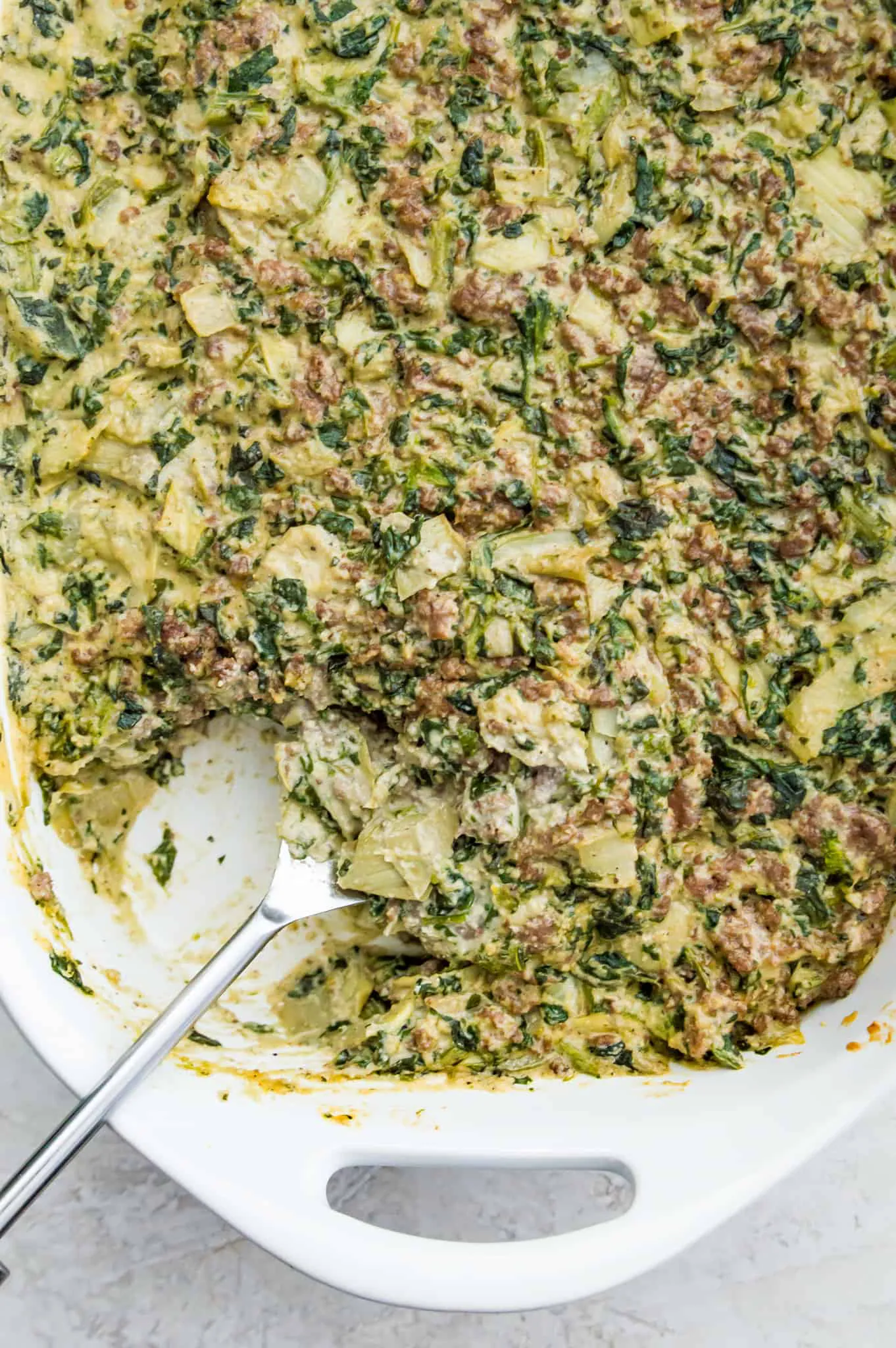 A pan of paleo spinach and artichoke casserole with a spoon in it