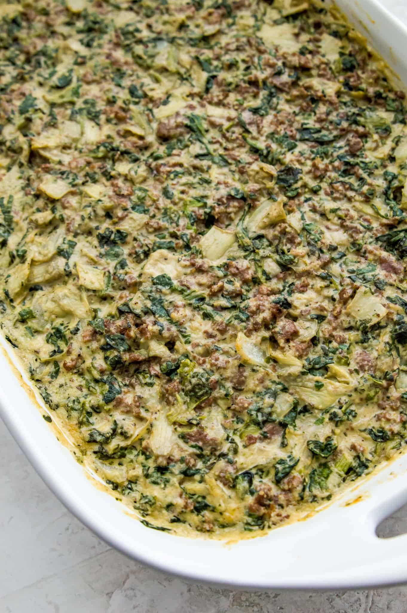 A casserole dish filled with a cooked spinach and artichoke casserole.