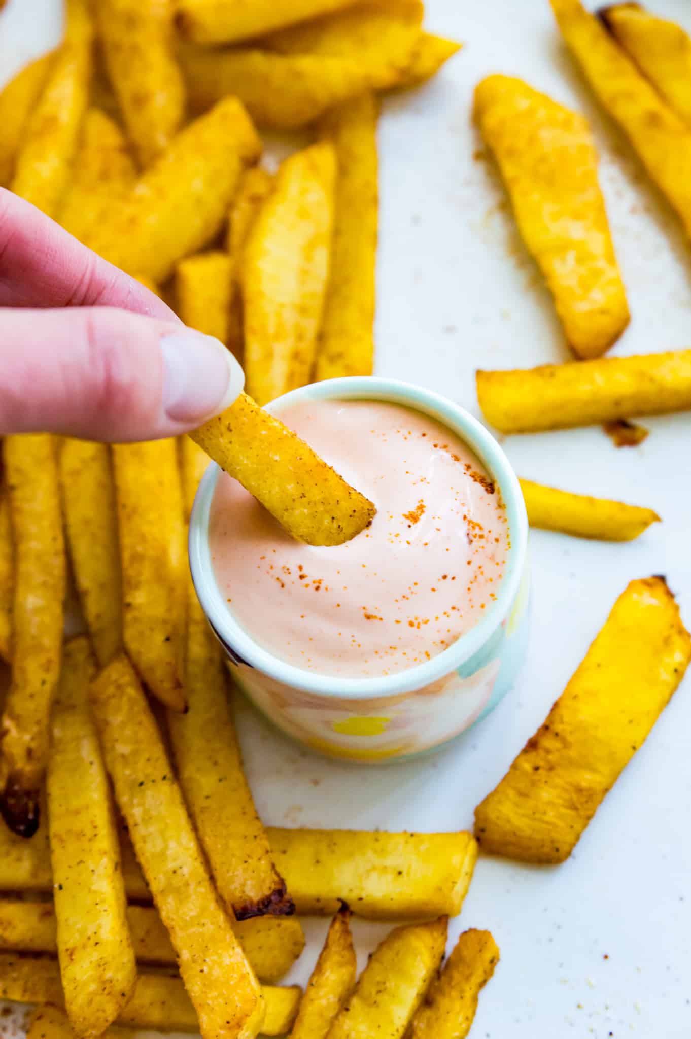 A small bowl of vegan sriracha mayo with a French fry being dipped into it.