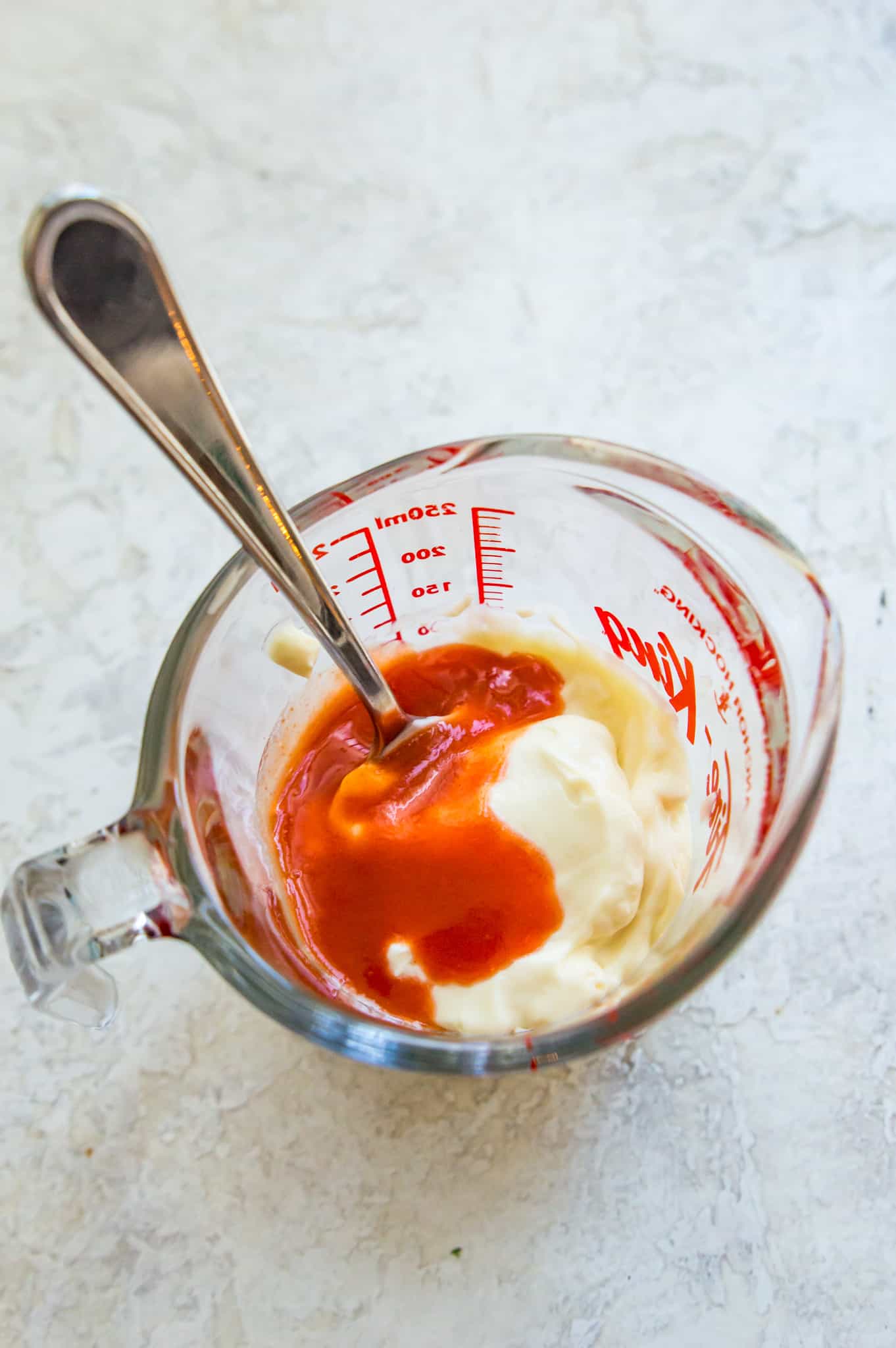 A measuring cup filled with ingredients for making sriracha mayo.