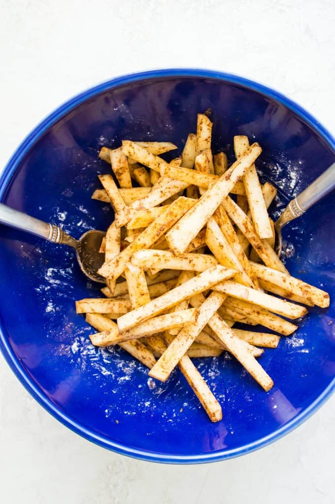 A bowl full of chopped turnips coated in seasonings. 